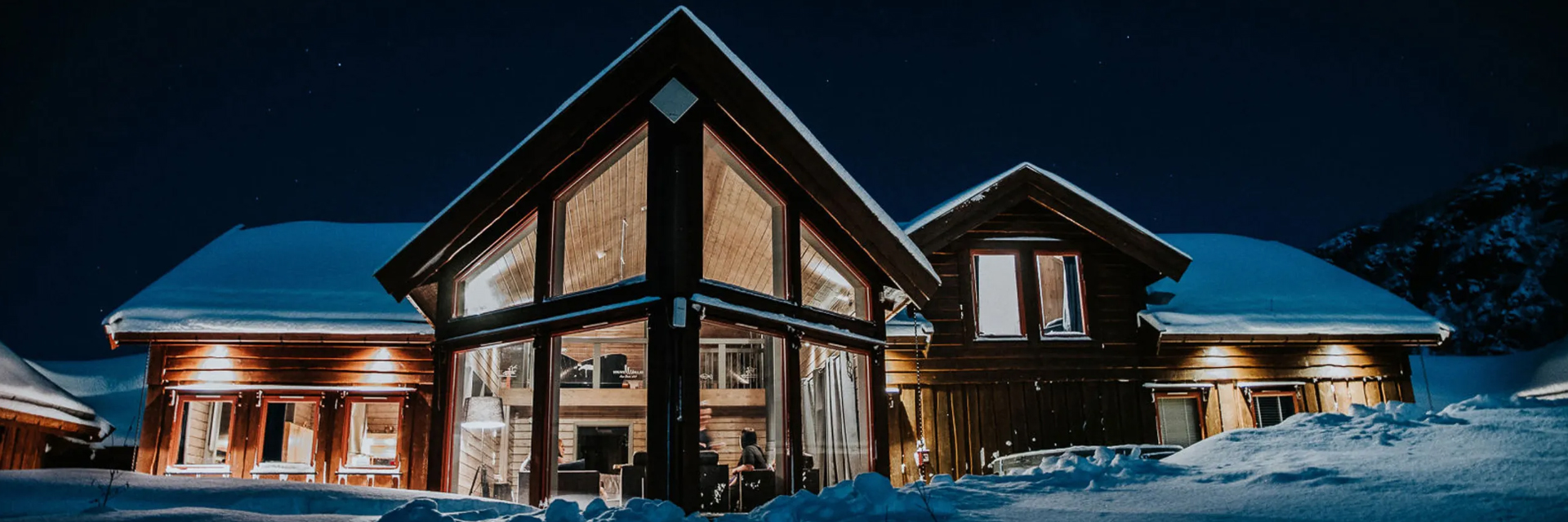 Wide view of Alten Lodge's main house glowing warmly at night in winter.