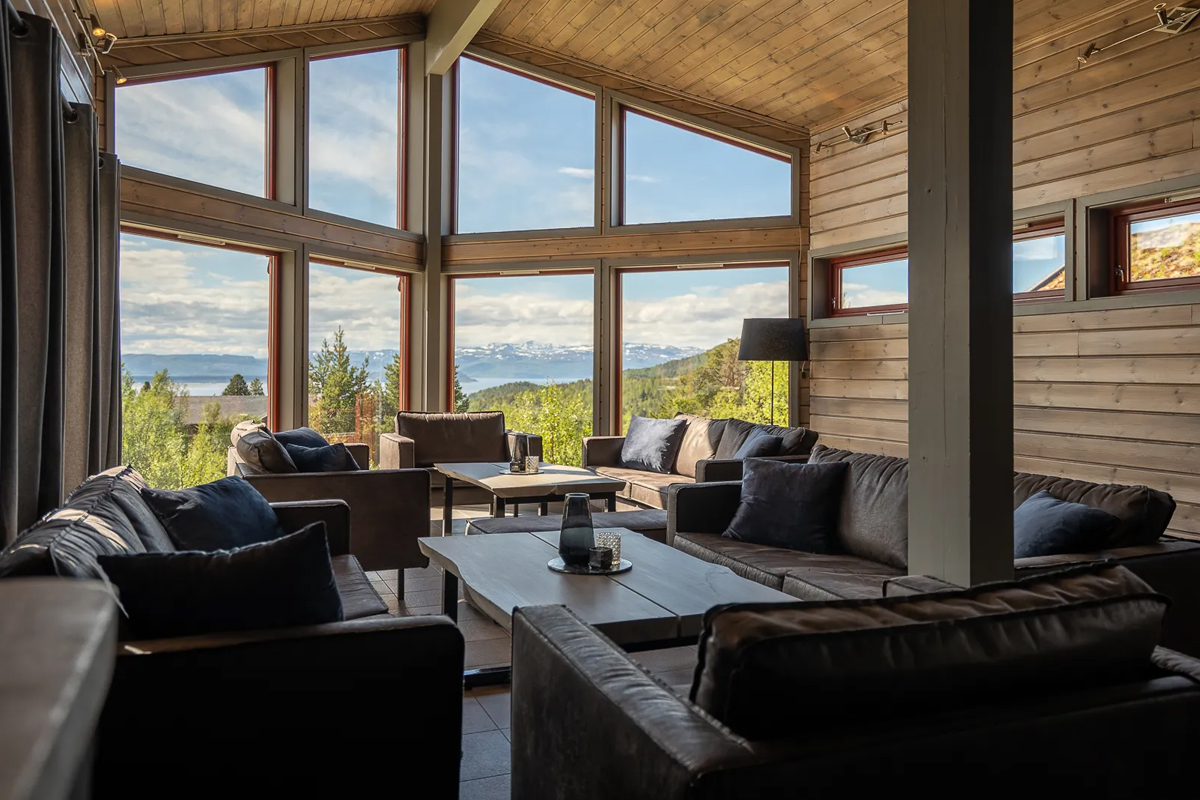 Main cabin lounge at Alten Lodge with tall windows overlooking the fjord in summer.