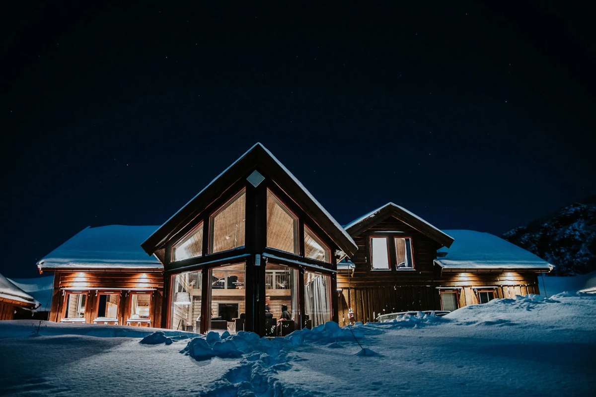 Alten Lodge main house lit up at night, surrounded by snow.