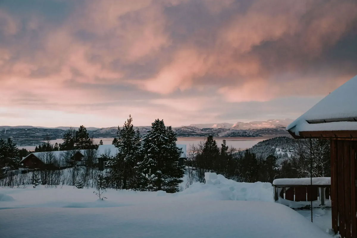 View of the fjord and mountains from Alten Lodge under a pink winter sunset sky.