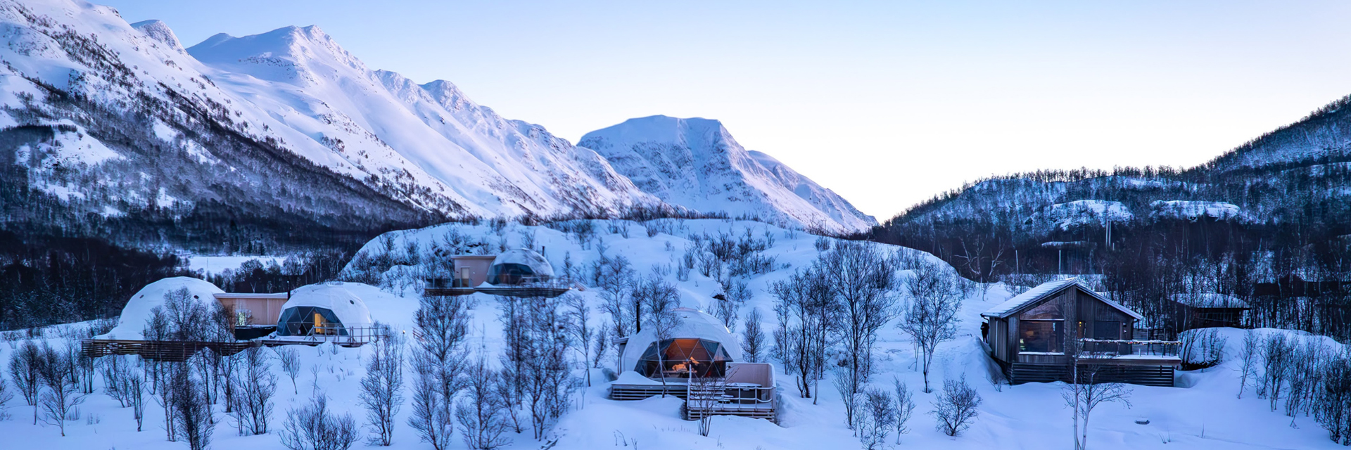 Panoramic view of Isbreen's igloos and cabins nestled among snowy peaks at dusk.