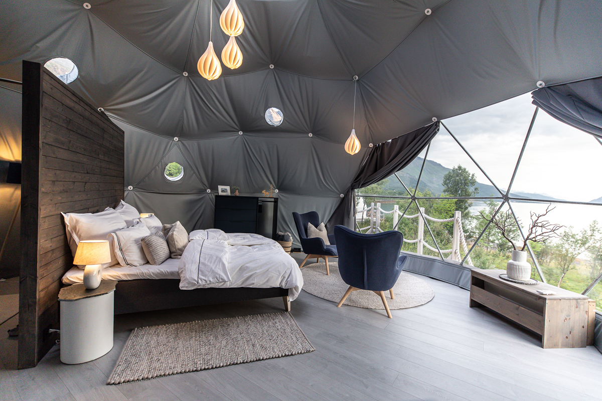 Bedroom and lounge area inside a spacious igloo at Isbreen, with fjord views through the glass.