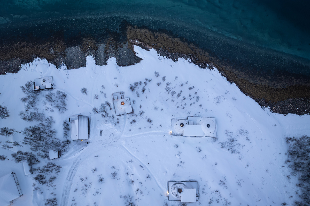 Aerial view of Isbreen's igloos and cabins scattered across a snowy shoreline at dusk.