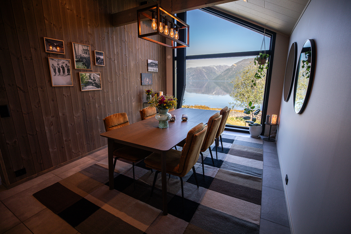 Dining room at Isbreen with a wood-paneled wall, long table, and fjord views through the window.