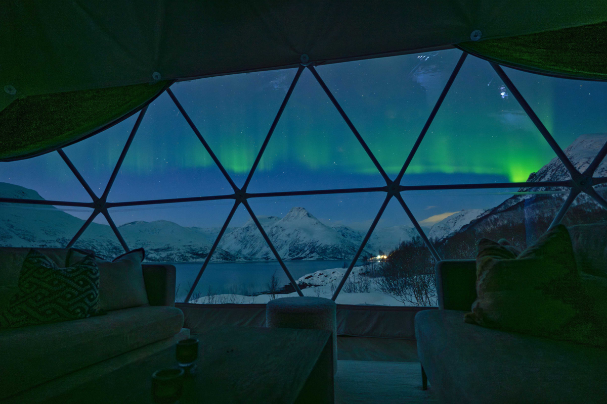 View of the northern lights over the fjord and mountains from inside an Isbreen igloo.