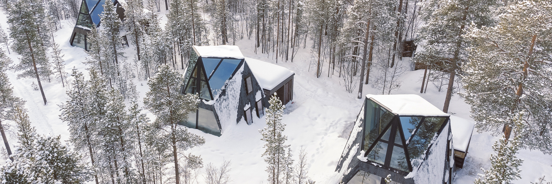 Aerial view of glass cabins at Trasti & Trine nestled among snow-covered pine trees.