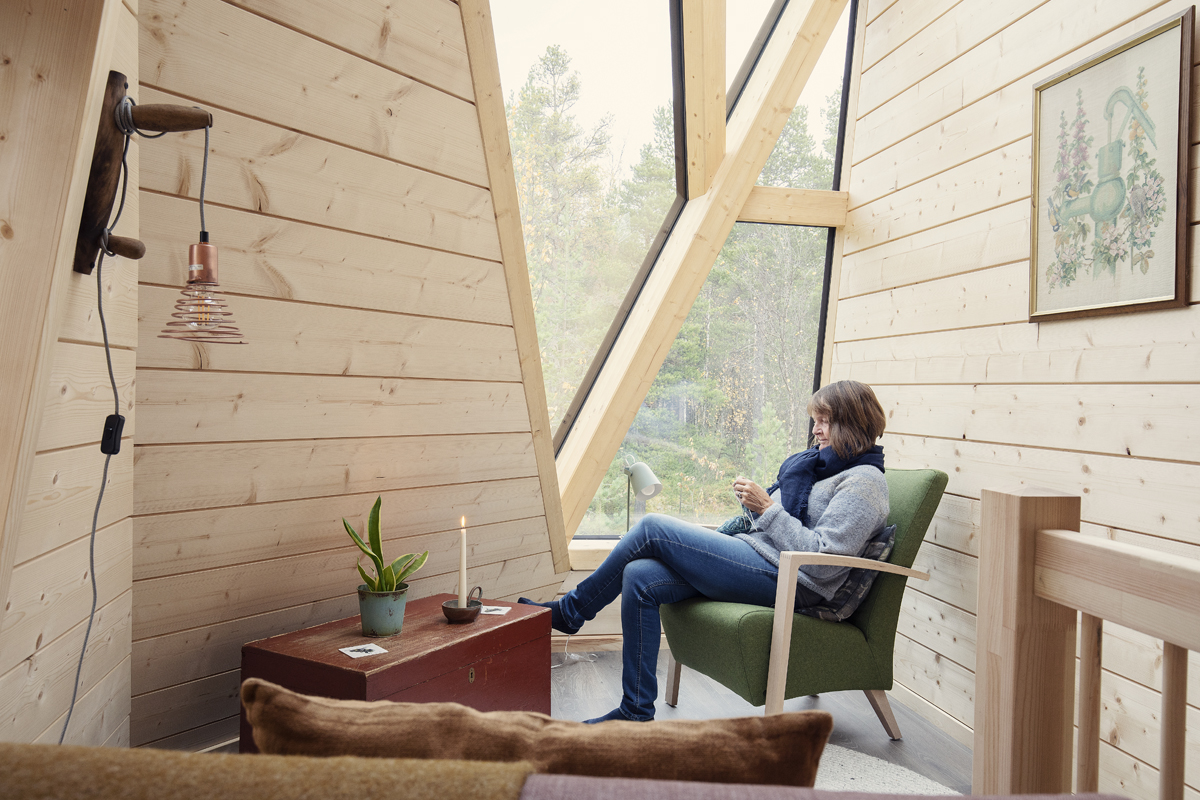 A guest relaxes by the window inside a wooden glass cabin at Trasti & Trine.