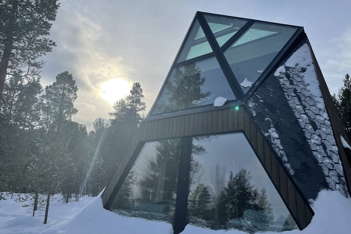 A-frame glass cabin exterior at Trasti & Trine surrounded by snowy pine forest.