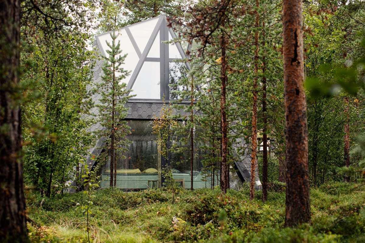Glass cabin at Trasti & Trine seen through summer forest greenery.