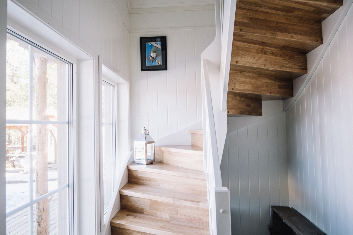 Wooden staircase inside the guest house at Trasti & Trine, with light streaming through the windows.