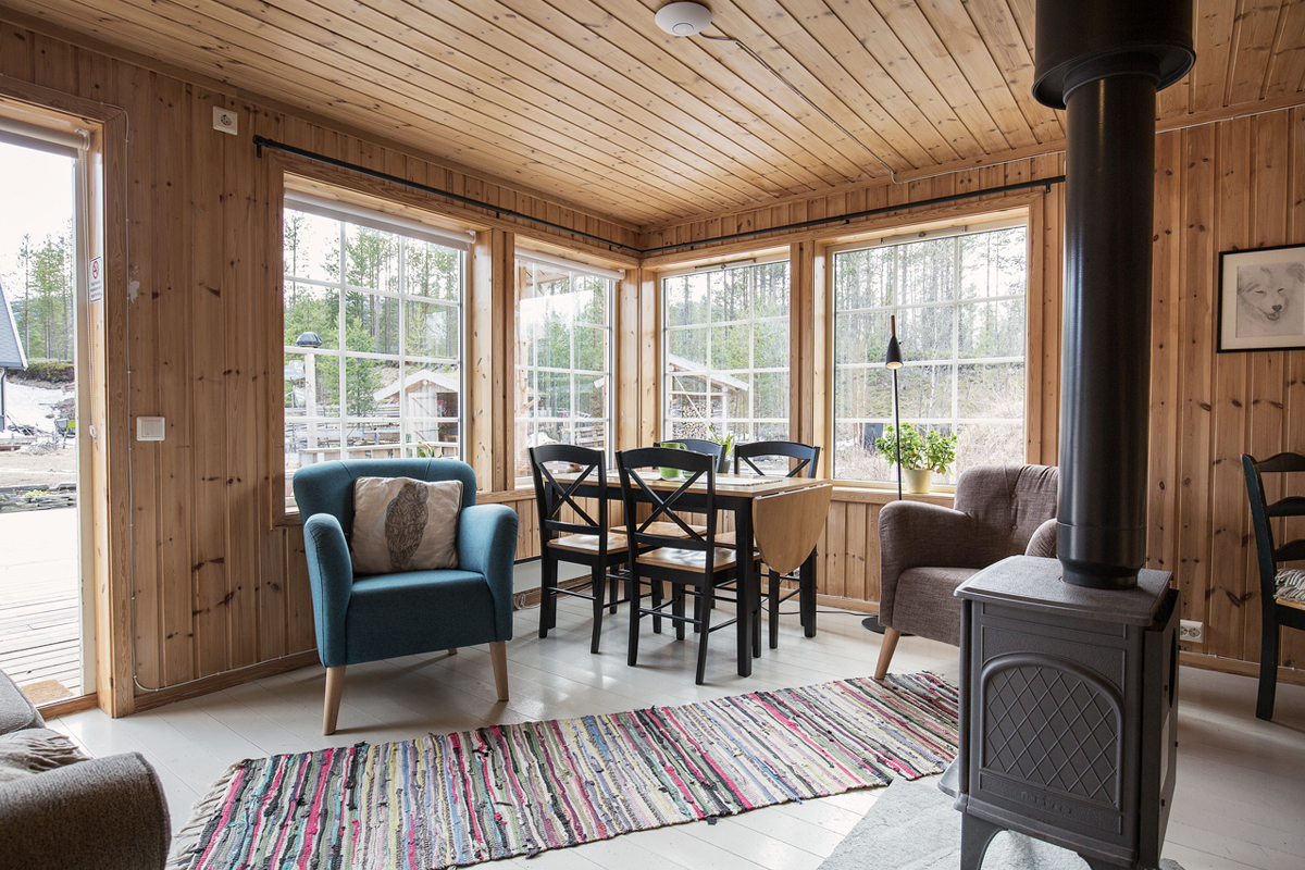 Wood-paneled lounge at the Trasti & Trine main house with a wood stove and forest views.