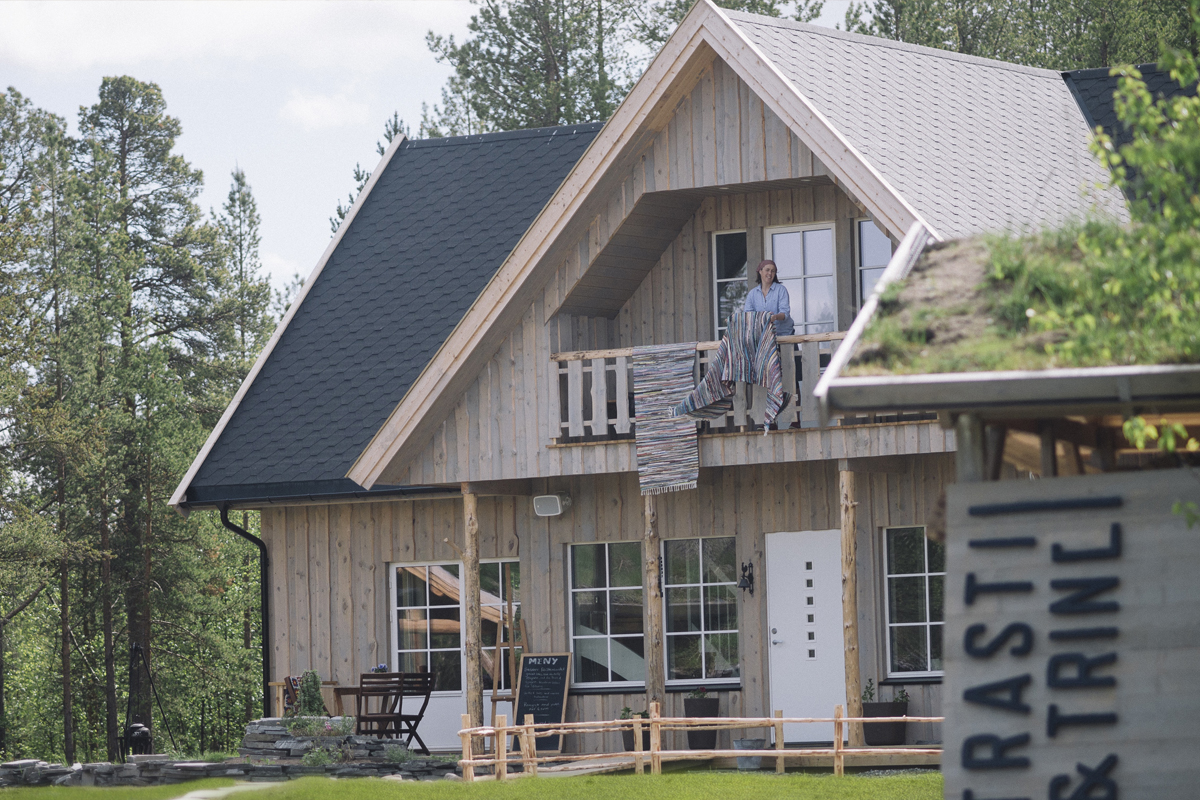 Exterior of the Trasti & Trine main house with a guest on the upper balcony.