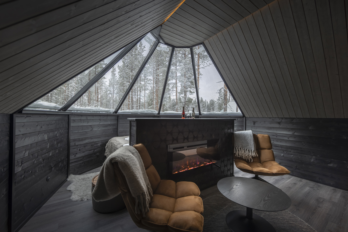 New cabin lounge with two armchairs, a fireplace and a large glass wall overlooking a snowy forest, Aurora Village, Ivalo