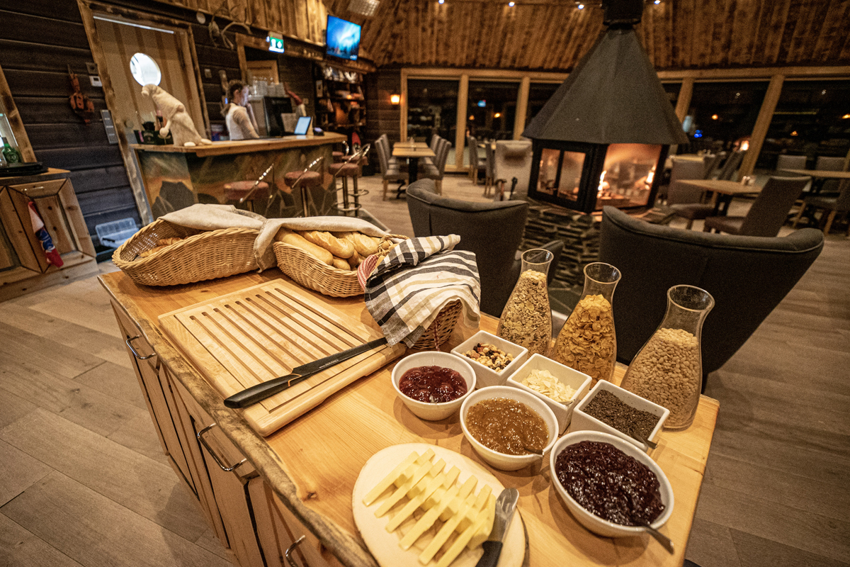 Breakfast buffet counter with bread baskets, jams and cereals beside the central fireplace, Aurora Village, Ivalo