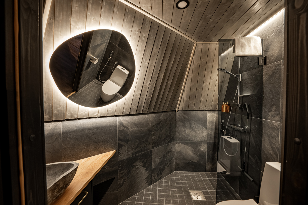 Tower suite bathroom with dark slate tiles, a round backlit mirror, stone basin and walk-in shower, Aurora Village, Ivalo