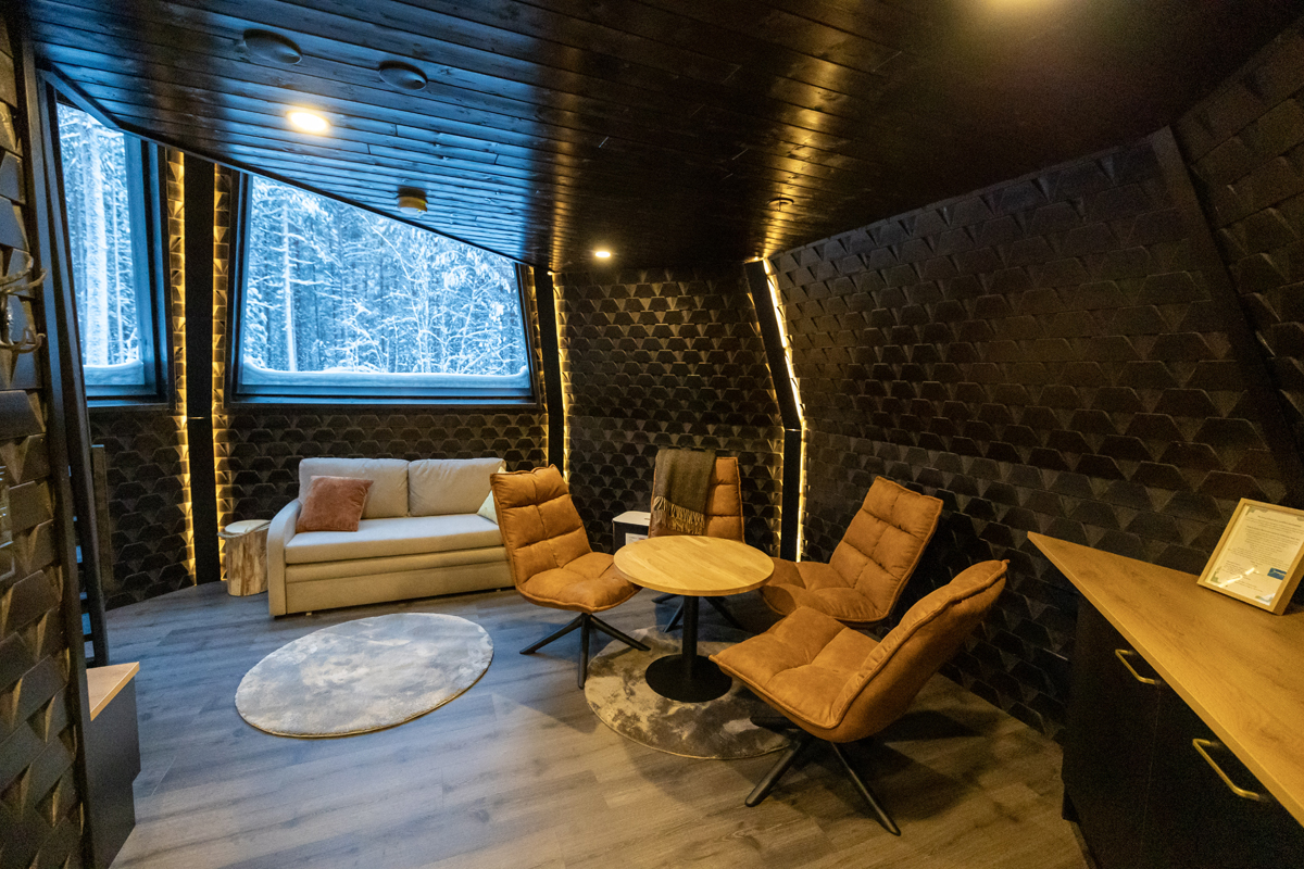 Tower suite lounge with amber armchairs, textured dark walls and a snowy forest view, Aurora Village, Ivalo