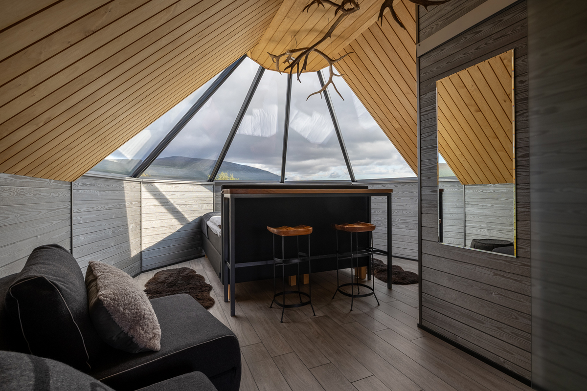 Inside a glass igloo cabin with a peaked window ceiling and small bar area at Arctic Land Adventure, Kilpisjärvi.