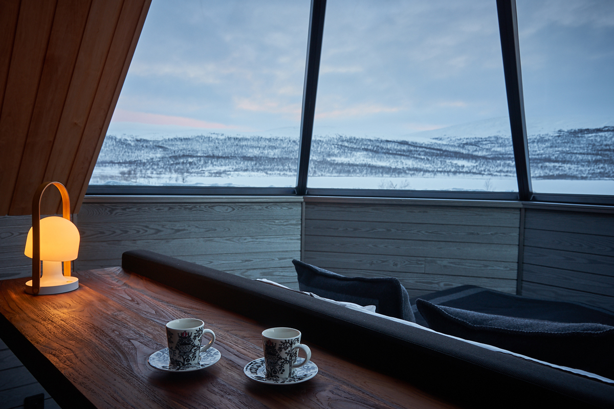Two coffee cups rest on a table inside a glass igloo overlooking snowy fells at Arctic Land Adventure.