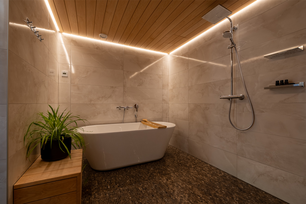 A freestanding bathtub and rain shower in the wood-ceilinged bathroom at Villa Vasara, Kilpisjärvi.