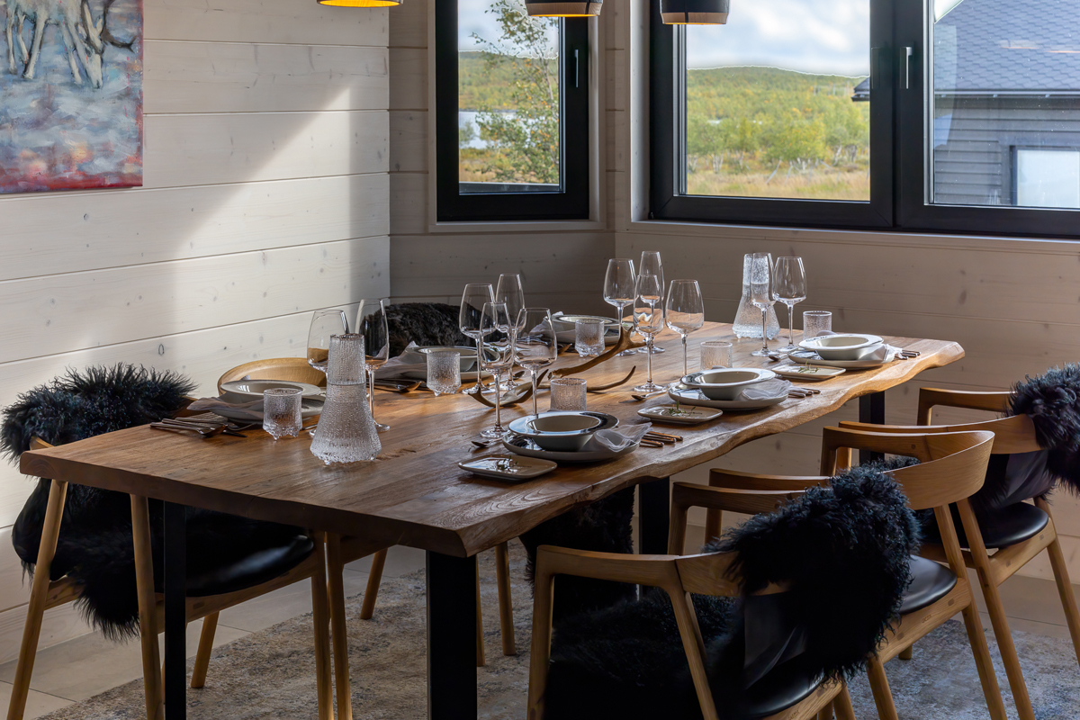A long dining table set for a group meal beside large windows at Villa Vasara, Kilpisjärvi.