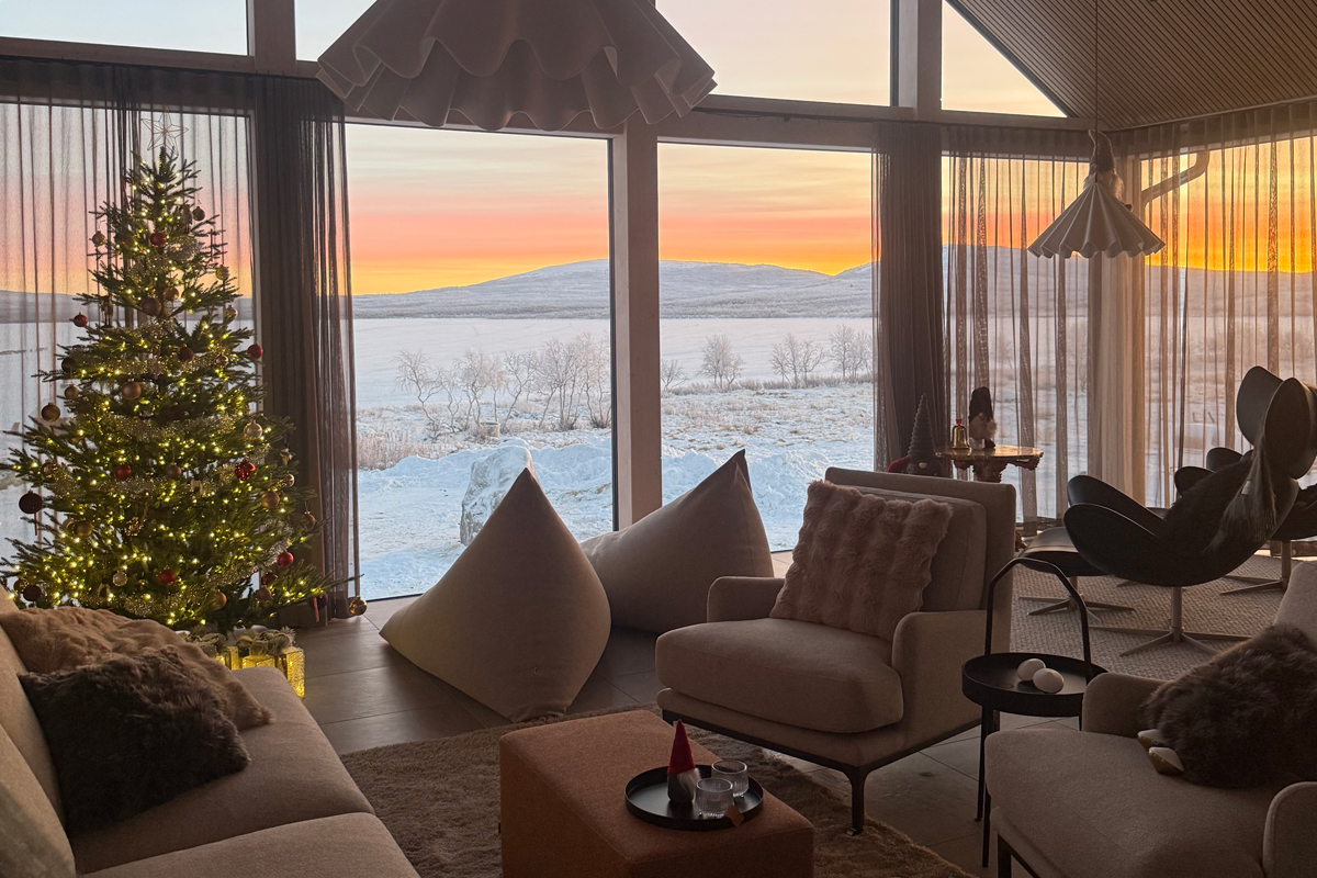 A Christmas-decorated lounge at Villa Vasara overlooks a snowy fell landscape at sunset, Kilpisjärvi.