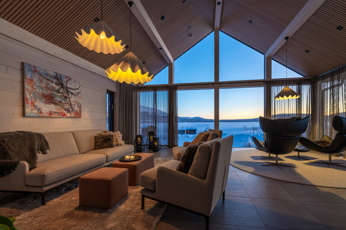 A spacious lounge with vaulted wood ceiling and panoramic lake views at Villa Vasara, Kilpisjärvi.