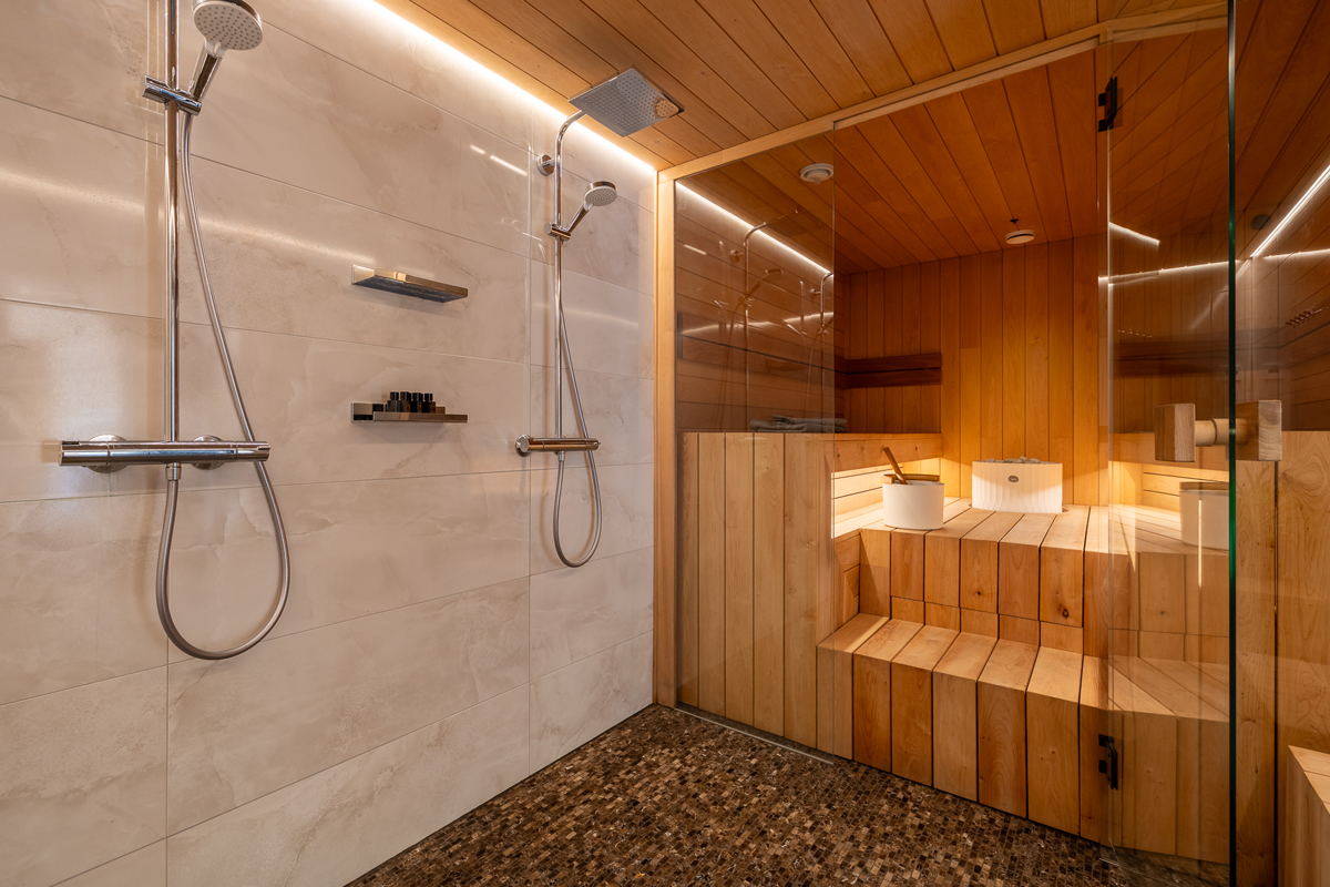 A glass-walled sauna beside a dual rain shower area at Villa Vasara, Kilpisjärvi.