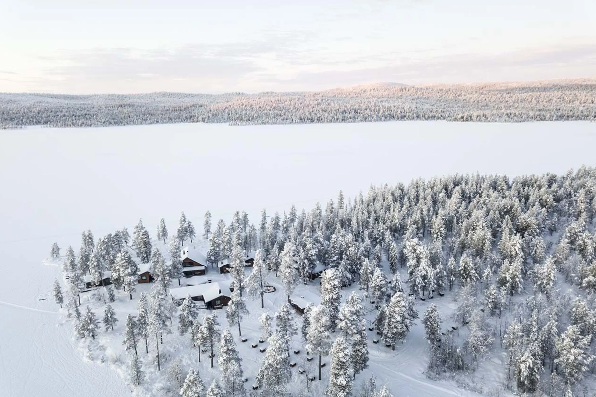 Aerial view of Fjellborg Arctic Lodge cabins nestled among snowy pines beside a frozen lake in Kiruna.