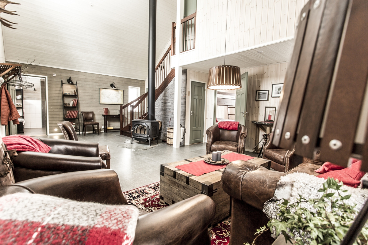 A double-height living room with leather armchairs, a wood stove, and a mezzanine at Fjellborg Arctic Lodge, Kiruna.