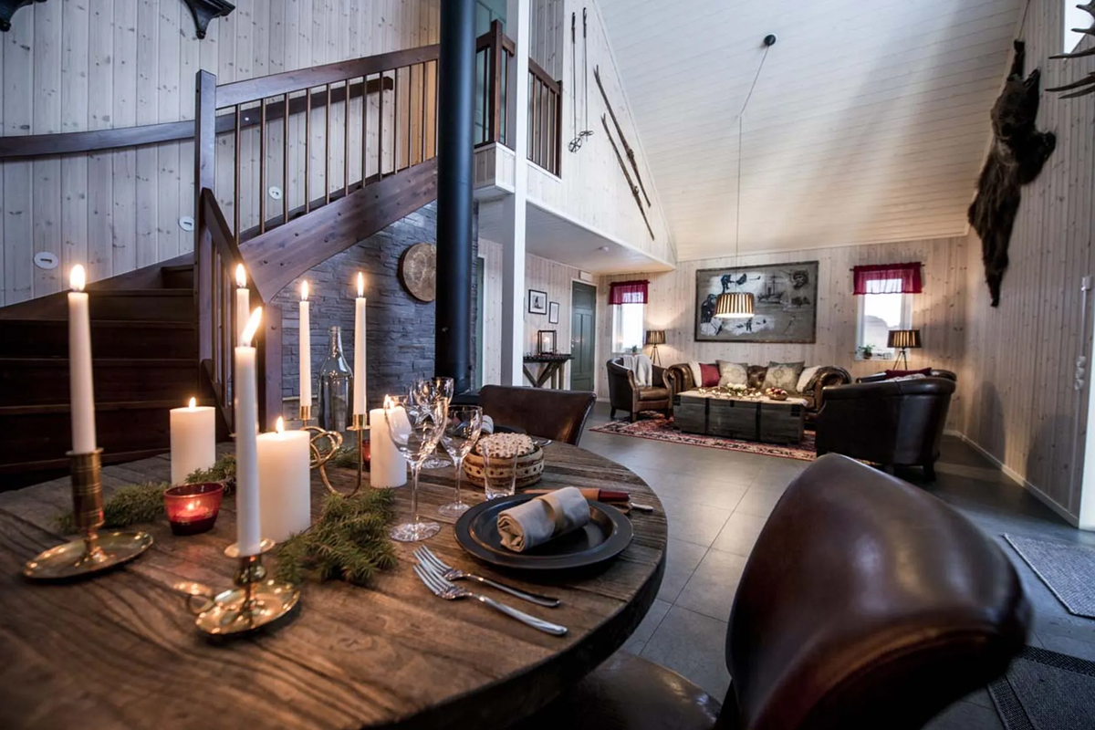 A candlelit dining table with a wood stove and staircase in the background at Fjellborg Arctic Lodge, Kiruna.