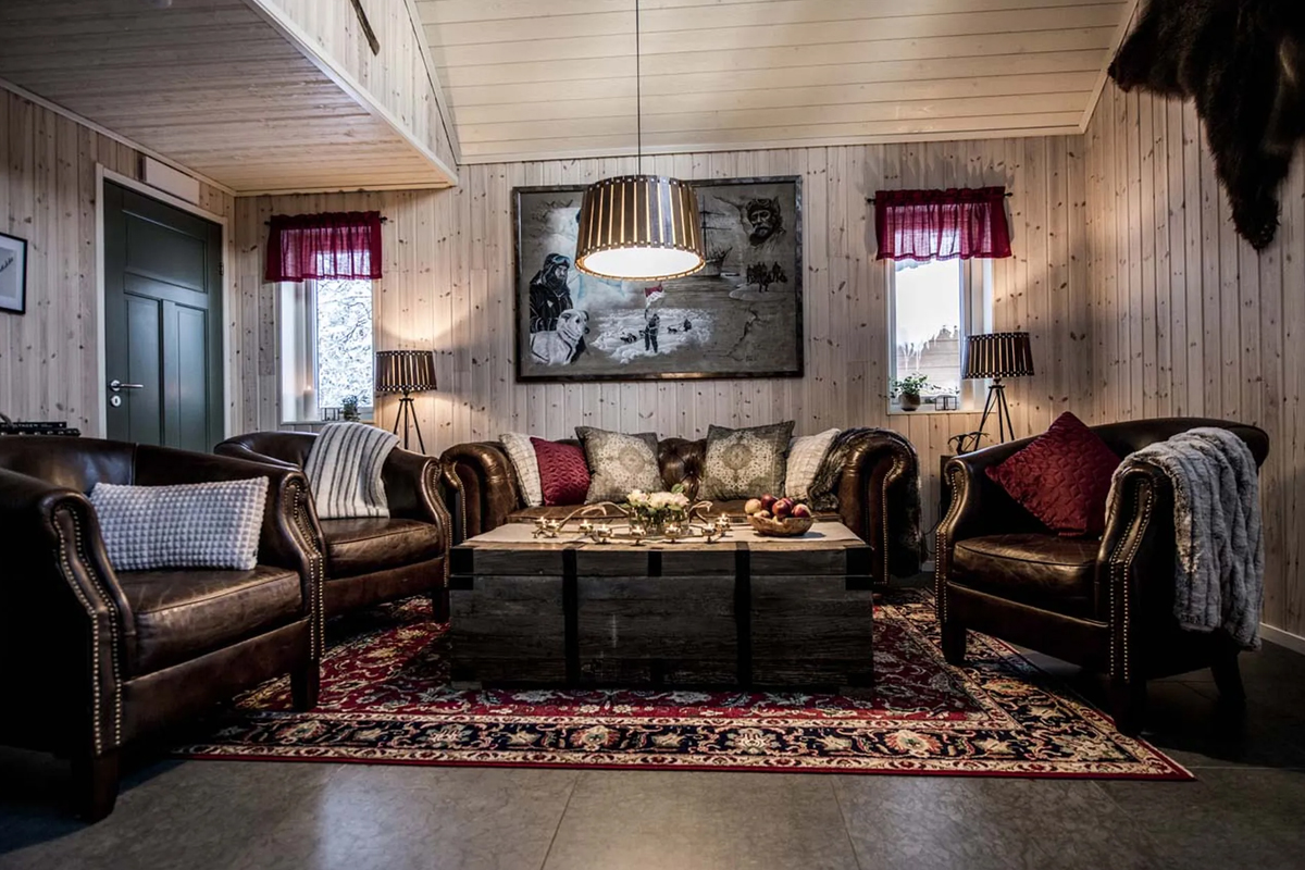 A leather-furnished lounge with a large framed artwork and patterned rug at Fjellborg Arctic Lodge, Kiruna.