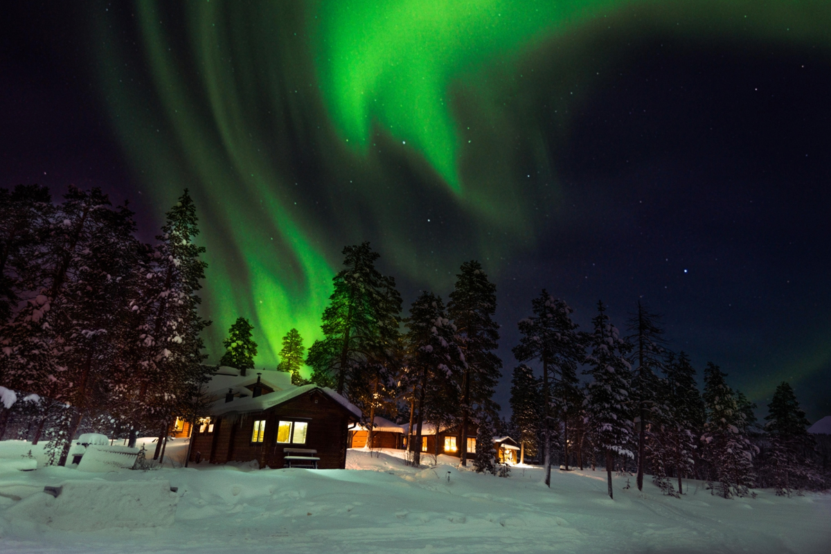 Vivid green northern lights swirl above a snow-covered cabin at Fjellborg Arctic Lodge in Kiruna.
