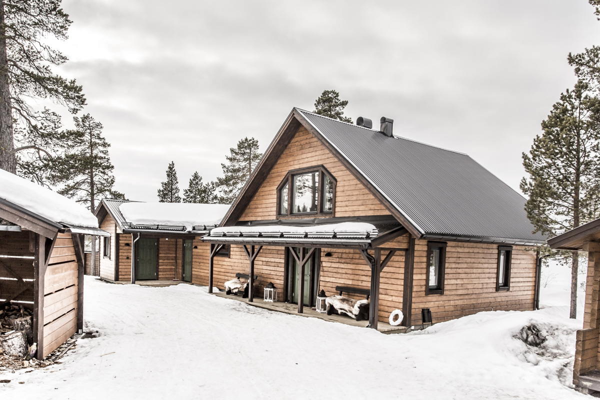 The timber exterior of Fjellborg Arctic Lodge with a covered porch and reindeer hides in snowy Kiruna.