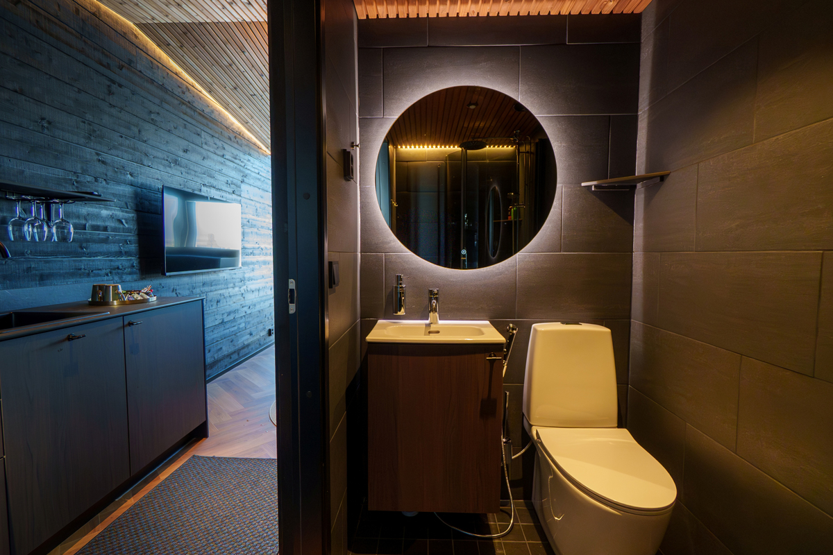 Bathroom inside an Aurora Room at Lumo Resort in Ruka, with round mirror and dark tiles.