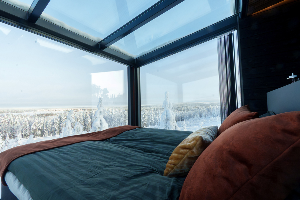 Bedroom with glass ceiling at Lumo Resort in Ruka, overlooking snow covered forest.