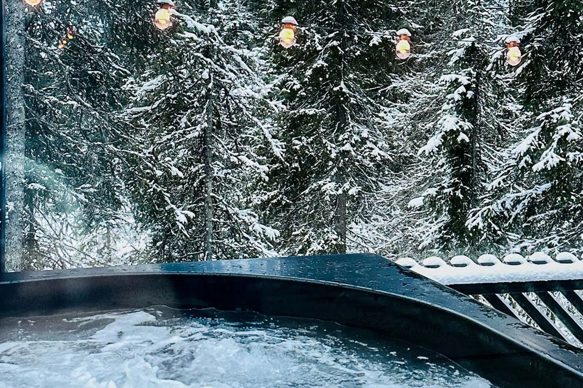 An outdoor hot tub at Magical Pond in Kuusamo, facing snow-laden pine trees and warm string lights in winter.