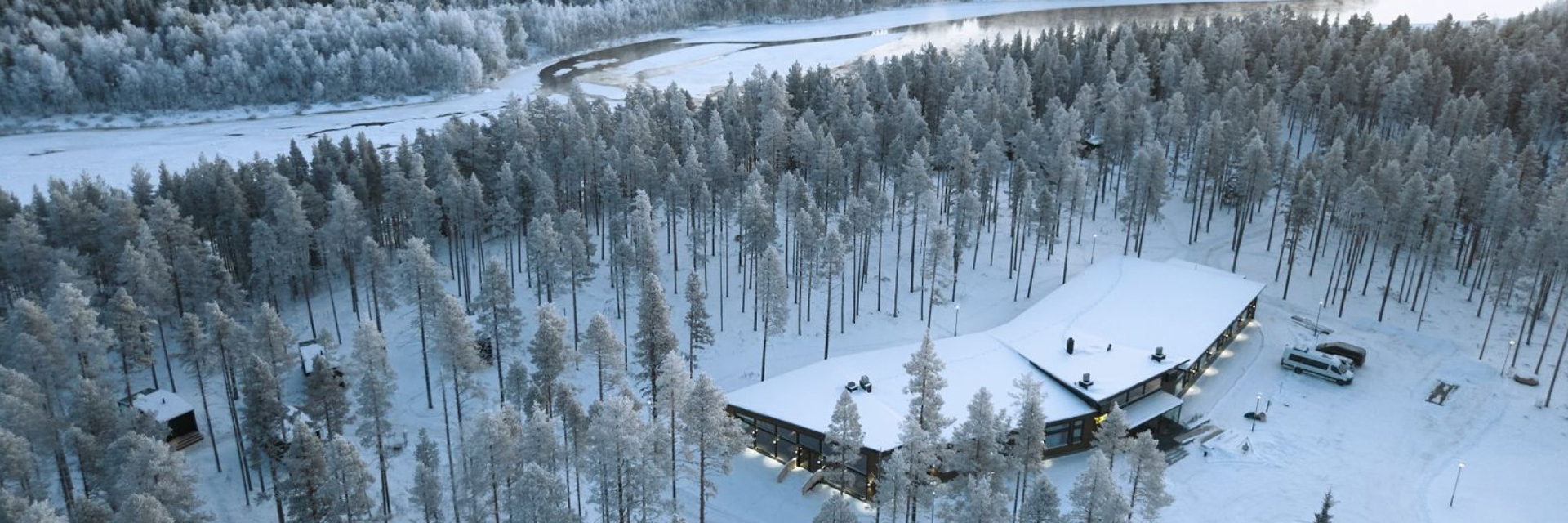Aerial view of Balder Luxury Lodge in Levi, with the river visible beyond the tree line.