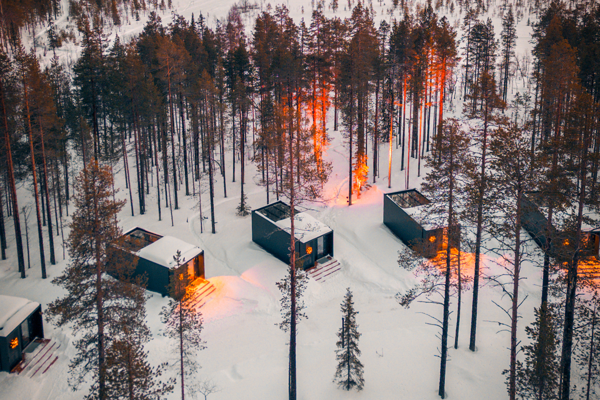 Aerial view of glass cabin rooftops at sunset among snow-covered pine trees, Olo Resort, Levi