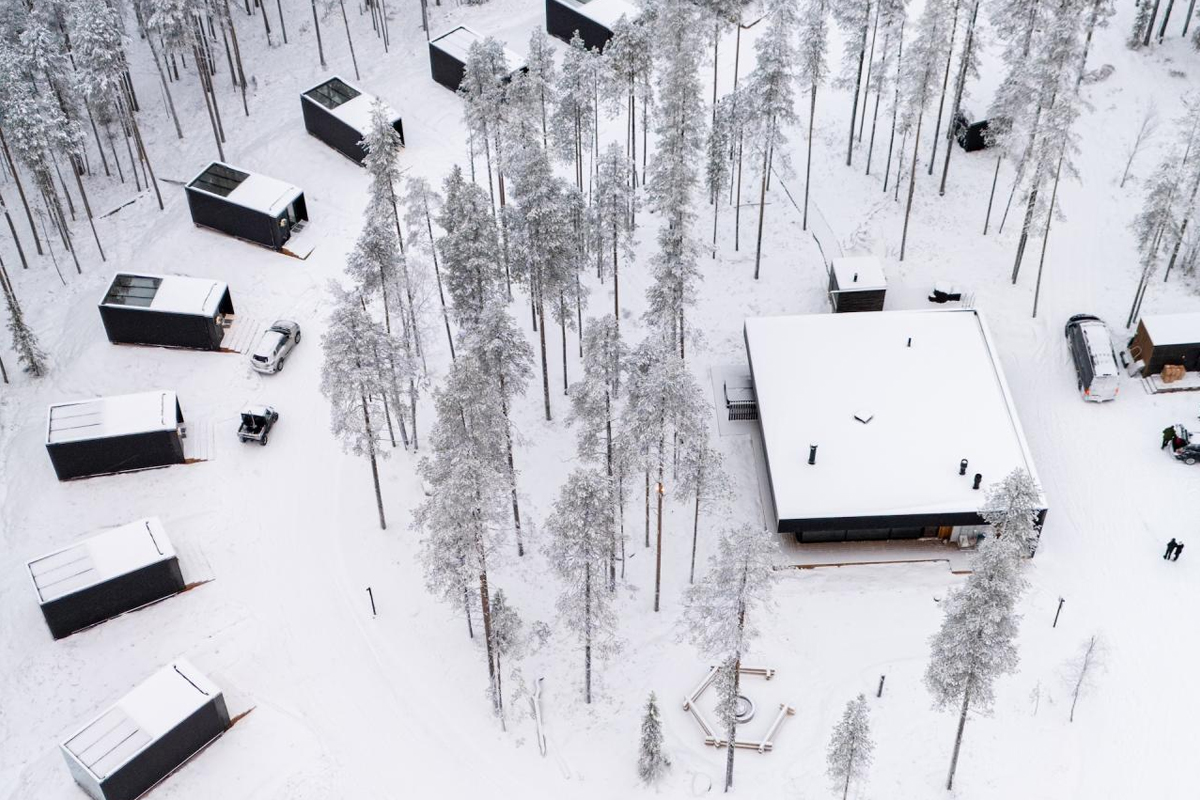 Aerial view of Olo Resort with dark glass cabins set among snow-covered pine trees and the main building, Levi