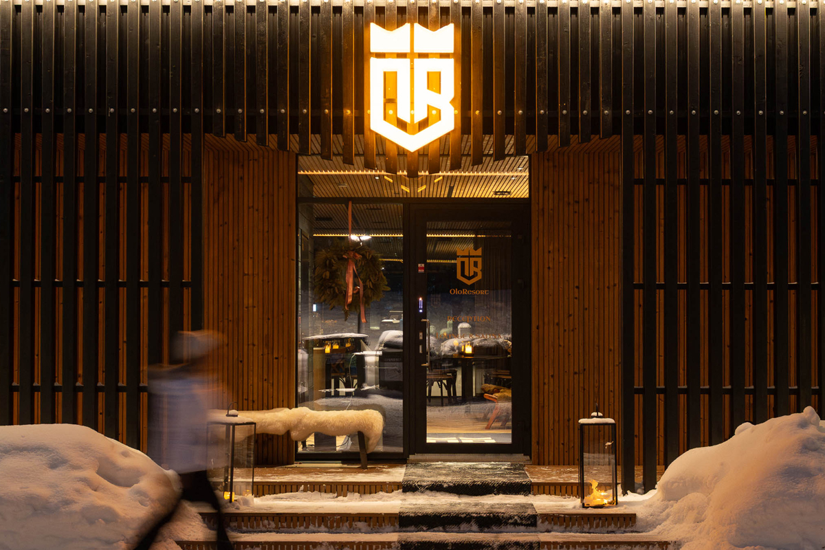Main entrance of Olo Resort at night with an illuminated logo and a wooden slatted facade, Levi