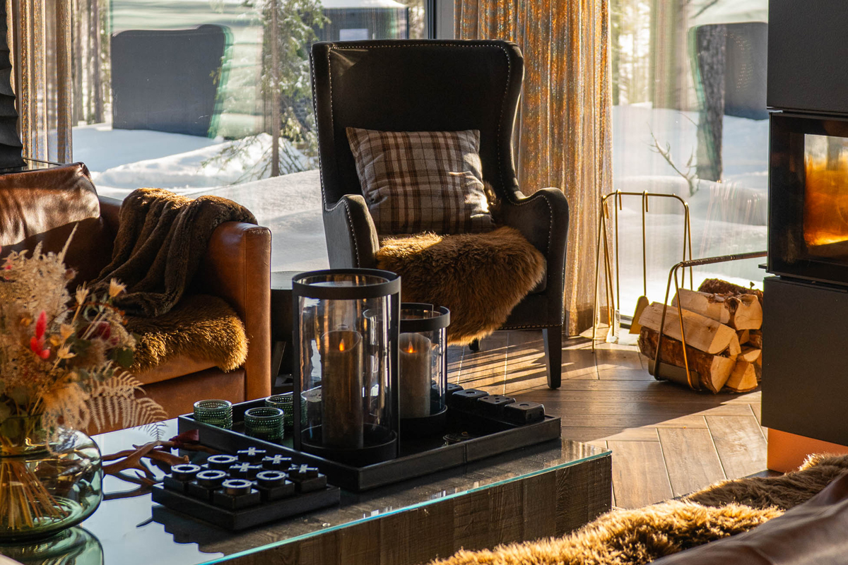 Lounge armchair with fur throw beside a lit fireplace and a snowy forest view, Olo Resort, Levi