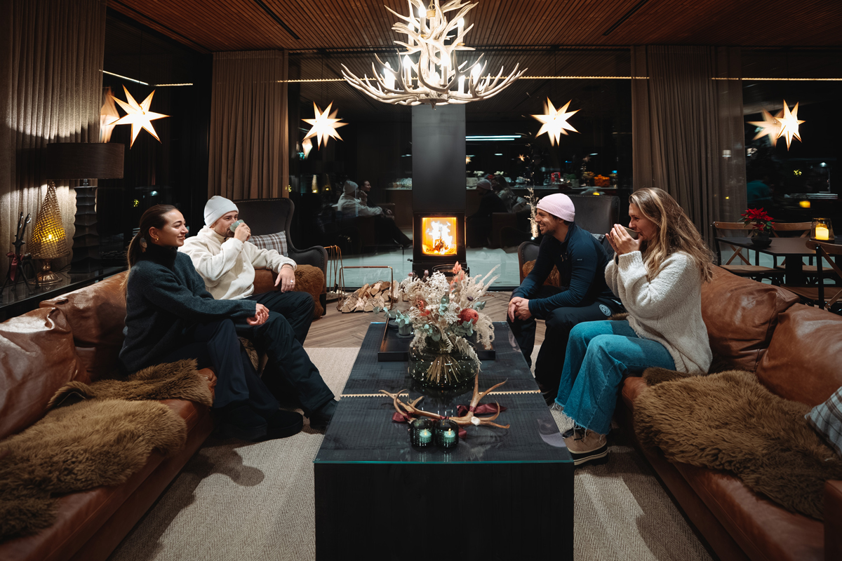 Group of four friends relaxing on leather sofas by a fireplace in the main lounge, Olo Resort, Levi