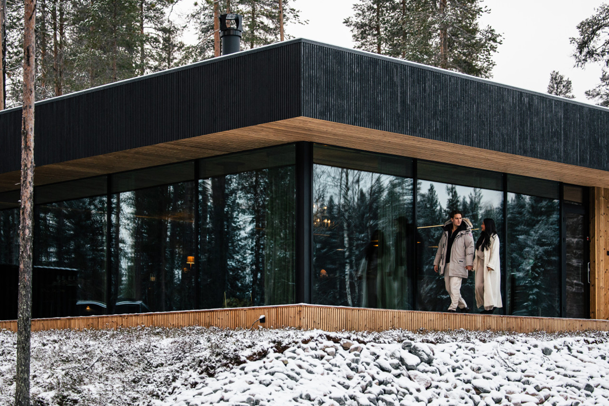 Couple walking on the terrace of the Olo Resort main building with a glass and wood facade, Levi
