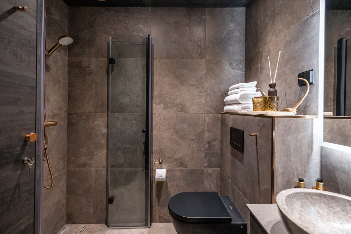 Glass cabin bathroom with dark stone tiles, a walk-in shower, black fixtures and copper fittings, Olo Resort, Levi