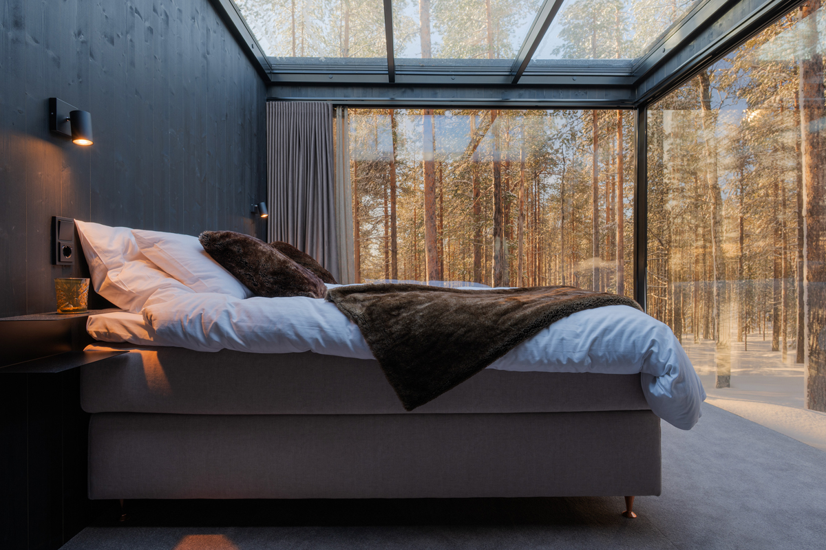 Double bed with fur throw in a glass cabin with floor-to-ceiling forest views at sunset, Olo Resort, Levi