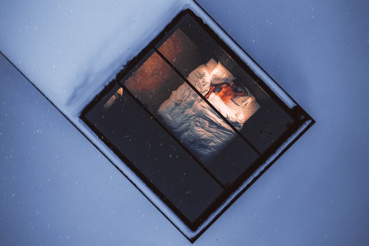 View through the glass ceiling of a cabin showing a guest lying in bed from above, Olo Resort, Levi