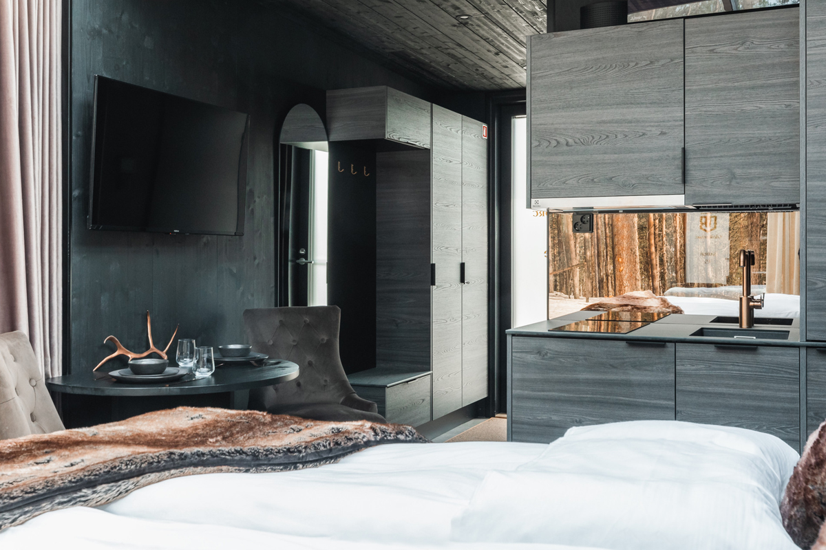 Glass cabin interior with a double bed, kitchenette, dining area and fur throws, Olo Resort, Levi