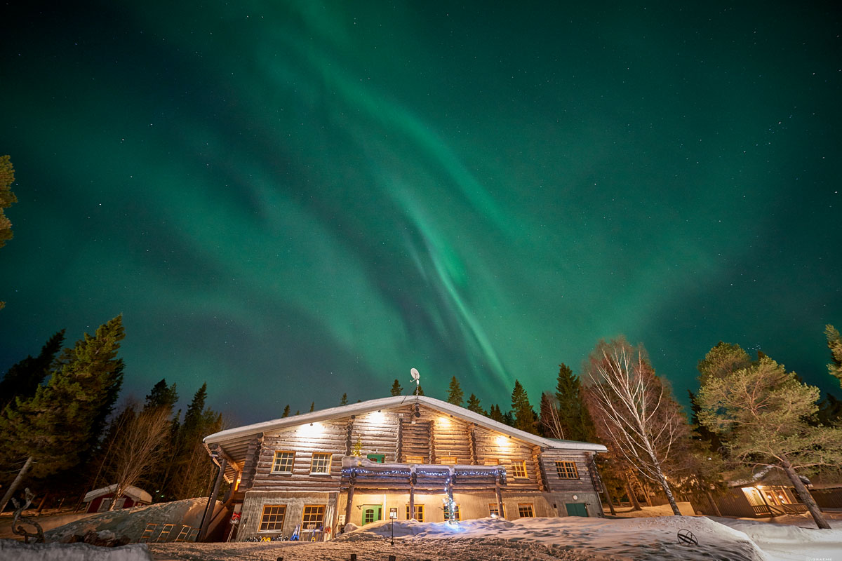 Log cabin restaurant at Brändön Lodge under the northern lights in winter, on the Luleå archipelago coast in Swedish Lapland.