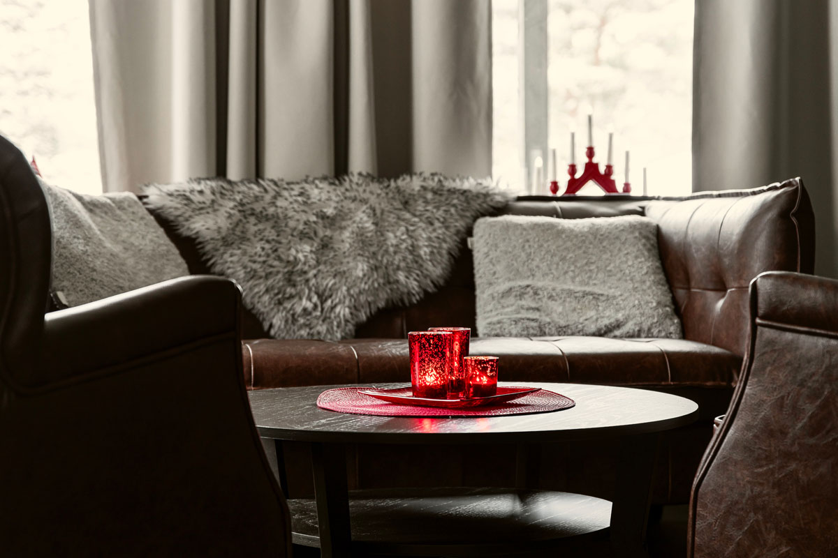 Cosy sitting area inside a cabin at Brändön Lodge in winter, with leather sofa, fur cushions, and candles on the table.