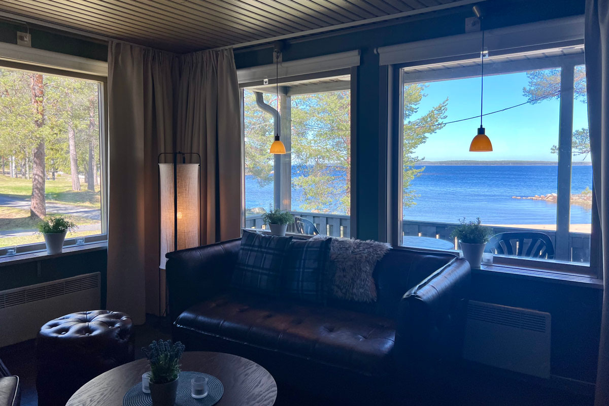 Living room in a cabin at Brändön Lodge in summer, with leather sofa and windows overlooking the sea and the Luleå archipelago.